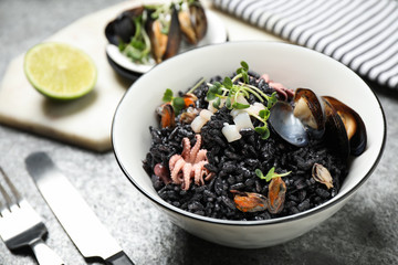Delicious black risotto with seafood in bowl on table