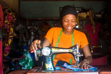 portrait of a young african female tailor smiling while working with her sewing machine