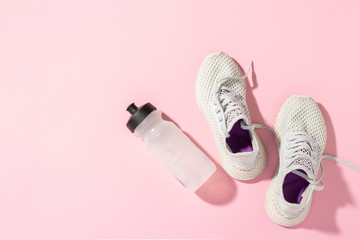 White sneakers and a bottle of water under morning sunlight on a pink background. Concept, jogging,...