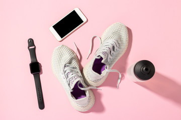 White running shoes, phone,a sports watch and a water bottle on a white background under the...