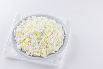 Cottage cheese in a white plate. Fresh cottage cheese on a white background. Homemade curd in minimalism style. Top view. Copy space