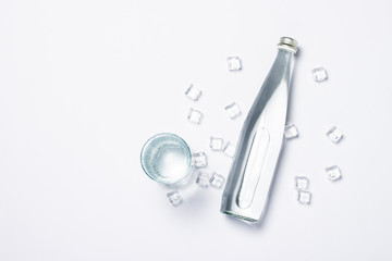 Bottle of pure crystal water with ice cubes and glass on a white background under sunlight. Banner. Concept of thirst, heat, summer, tropic. Flat lay, top view
