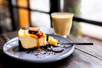  Slice of cheesecake with a cup of coffee on a wooden table. Cheesecake with nuts and caramel. Snickers cheesecake. Caramel Pie. Slice  caramel cheesecake with popcorn. Dessert with latte in a glass