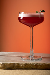 Red cocktail with foam, orange background.