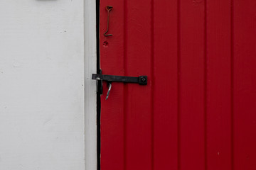 A red painted wood door with an antique hook and latch. Both items are a black vintage metal. The...