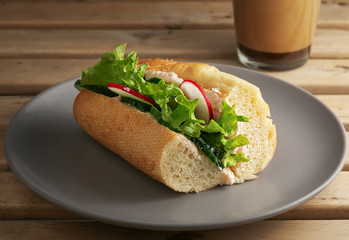 Sandwich with fresh vegetables on a ceramic gray plate. Wooden brown background. A cup with coffee in the background. Vegetarian sandwich. Close-up.