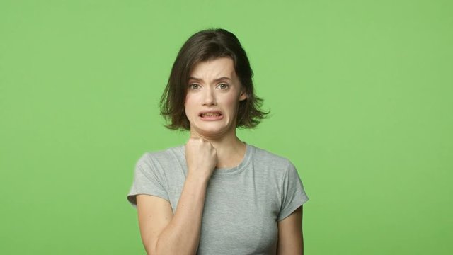 Slow-motion, frustrated and shocked nervous young woman hear bad news, frowning, cringe and grimacing worried, hold hand near mouth startled, worry, feeling alarmed over green background