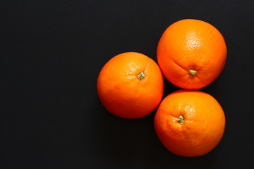 Three healthy oranges together on a dark surface, with copy space