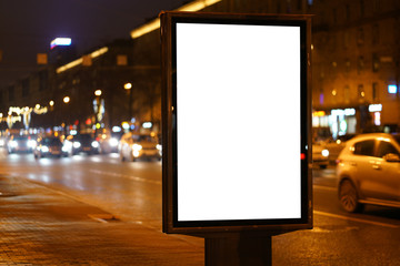 Mockup vertical billboard standing in city city format. Glowing at night billboard with an advertising field. with cars passing by blurry