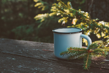 Enameled cup of coffee or tea on wooden board in summer forest outdoors.