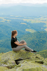 Naklejka na ściany i meble Young woman sitting on a rock and looking to the horizon.