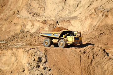 Big yellow dump truck transporting sand in an open-pit mining quarry. Mining quarry for the production of crushed stone, sand and gravel for use in the construction industry - image