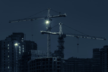 Construction cranes with LED lighting on a construction site on a winter night. Toned photo