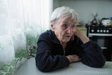 An old woman sitting in the kitchen of her apartment.