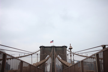 Waving flag of the United States on top of a tower of the Brooklyn Bridge at bad cloudy weather