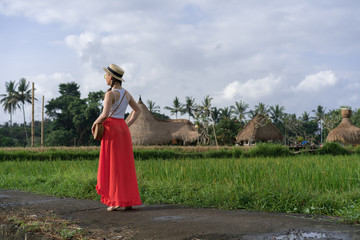 Beautiful young woman in red long maxi skirt with  straw hat and bag. Girl travel in Ubud, Bali, Indonesia