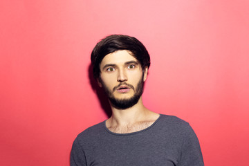 Portrait of young surprised man on pink coral background.