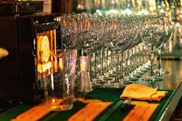 Empty wine glasses on the bar in a dark room, lined up in rows.