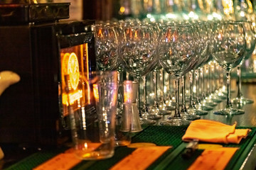 Empty wine glasses on the bar in a dark room, lined up in rows.