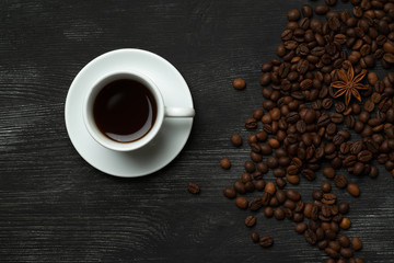 White cup with coffee on a black background with coffee beans and anise star  top view