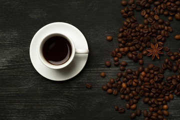 White cup with coffee on a black background with coffee beans and anise star  top view