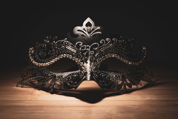 A portrait of a traditional venetian mask on a wooden surface appearing mysteriously out of the...
