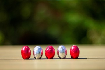 A portrait of chocolate easter eggs wrapped in tin colorful foiln standing up on a table ready to be found and eaten by children on their egg hunt.