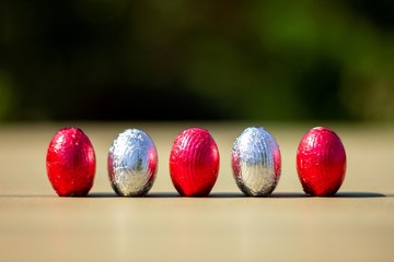 A portrait of chocolate easter eggs wrapped in tin colorful foiln standing up on a table ready to be found and eaten by children on their easter egg hunt.