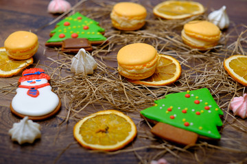 Christmas present set with sweets and oranges. Macaroons, gingerbread cookies set with snowman on wooden background. Vintage winter postcard.