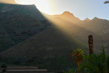 Rayos de sol sobre las montañas verdes y con palmeras - obrazy, fototapety, plakaty