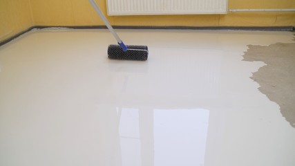 leveling the floor with a roller. The interior of the apartment is under construction....
