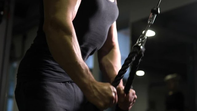 Male athlete pulling down rope on cable machine, pumping-up triceps and biceps