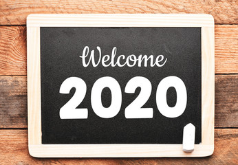Welcome 2020 text on a chalkboard and wooden background. New year 2020 concept.