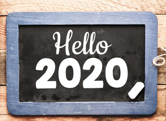 Hello 2020 text on a chalkboard and wooden background. New year 2020 concept.