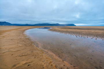Raudasandur or red sandy beach in the westfjords of Iceland during blue hour. Waves crash into the red sandy dunes at low tide. Texture in the foreground and mountains in the background. 