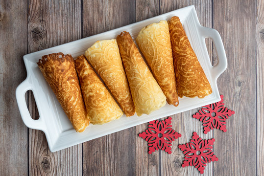 Norwegian Krumkake cookies on a white ceramic plater, rustic wood background, red snowflakes
