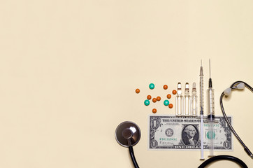 flat lay of medical supplies, stethoscope, syringe, ampoule, tablet on american dollar banknote...