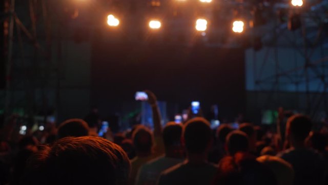 Audience at indoor music festival. Crowd enjoy rap concert, dancing in nightclub, people applauding to musician band, night entertainment. Silhouettes of concert crowd in front of bright stage lights