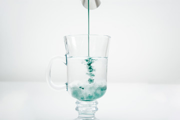 Pouring mint syrup into a glass of water. Beautiful green water color. Pouring the green dye into the water. The concept of preparing drinks.