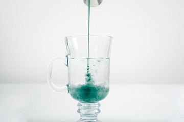 Pouring mint syrup into a glass of water. Beautiful green water color. Pouring the green dye into the water. The concept of preparing drinks.