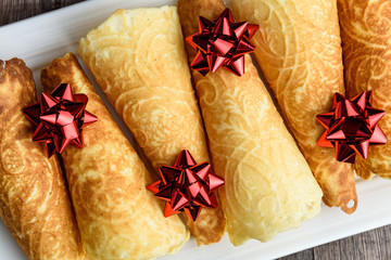 Norwegian Krumkake cookies on a white ceramic plater, rustic dark wood background, red ribbon bows