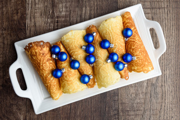 Norwegian Krumkake cookies on a white ceramic plater, rustic dark wood background, small blue Christmas balls