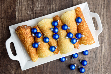 Norwegian Krumkake cookies on a white ceramic plater, rustic dark wood background, small blue Christmas balls