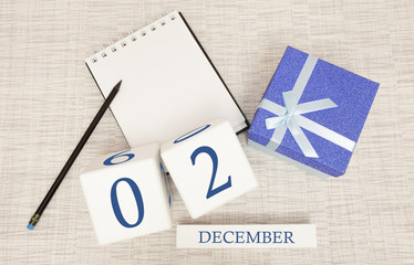 Cube calendar for December 2 and gift box, near a notebook with a pencil