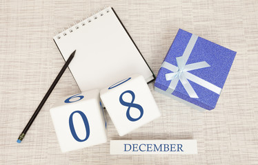Cube calendar for December 8 and gift box, near a notebook with a pencil