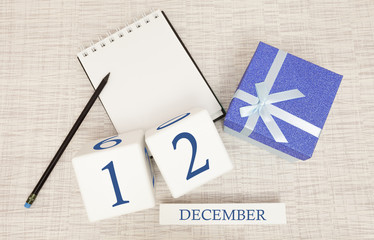 Cube calendar for December 12 and gift box, near a notebook with a pencil