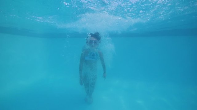 Child girl in swimming mask jumping in pool bathing in slow motion in tropics.
