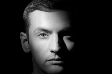 black and white dramatic portrait of a guy close-up on a black background with one light source - Powered by Adobe