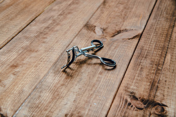 Scissors for attaching eyelashes on a wooden table. The concept of doing makeup, caring for the appearance of women. Applying brushes, eye shadows, powder.
