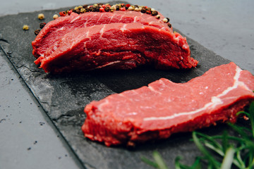 Raw beef, beef steak on a stone countertop, background with rosemary and spices. The concept of preparing a meal and eating. Fresh red beef, preparing a steak, using meat with a meal.